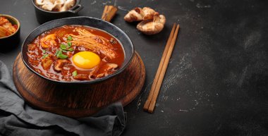 Baharatlı kimçi jjigae çorbasını yumurta sarısı, enoki, shiitake, tofu ve yeşil soğanlı, çubuklu ve pişirme malzemeli, Kore mutfağında, fotokopi alanında