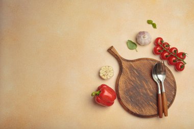 Kiraz domatesleri, kırmızı dolma biber ve taze fesleğen yaprakları açık bej desenli arka planda sade bir ahşap kesim tahtasına yerleştirilmiş.