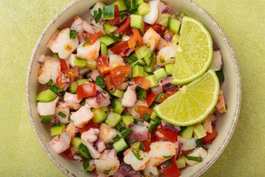 Taze ve canlı Peru deniz ürünleri ceviche ile karides, ahtapot, domates, salatalık ve maydanoz, yukarıdan açık yeşil bir arka planda limonla servis edilmiş, Peru yemeği.