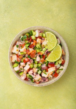 Taze ve canlı Peru deniz ürünleri ceviche ile karides, ahtapot, domates, salatalık ve maydanoz, yukarıdan açık yeşil bir arka planda limonla servis edilmiş, Peru yemeği.