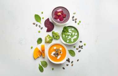 Üç farklı kase sağlıklı krema çorbası, bezelye yeşili, turuncu balkabağı ve kırmızı pancar, taze malzemelerle beyaz arka plan