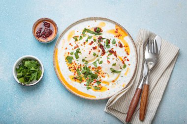 Türk yumurtaları cilbir, lezzetli ve renkli bir kahvaltı yoğurt üzerinde haşlanmış yumurta, baharat ve taze otlarla tatlandırılmış, mavi arka planda düzenlenmiş