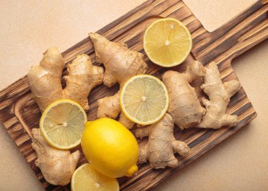 Zencefil kökleri ve dilimlenmiş limonlar sade ahşap bir kesim tahtasına dizilmiş, sağlıklı malzemeler hazırlıyorlar açık bej arka plan