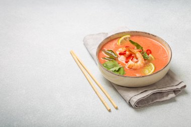 Taze karides, limon kamaları, şifalı otlar ve kırmızı biberlerle süslenmiş ve yanında keten peçetede yemek çubukları bulunan Tayland 'ın popüler bir yemeği olan kremalı Tom yum çorbası bir kâse içinde servis edilir.