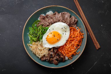 Bibimbap, haşlanmış pirinçli otantik Kore yemeği, kızarmış yumurta, sığır eti, renkli sebzeler, Kore 'nin geleneksel siyah arka plan manzarası.