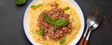 Lezzetli spagetti bolonez taze fesleğen ve rendelenmiş parmesan ile süslenmiş, beyaz tabakta servis edilen mavi kenarlı geleneksel İtalyan makarnası.