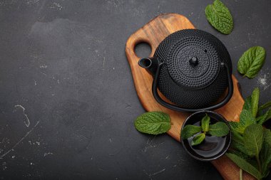 Geleneksel dökme demir çaydanlık ve kase sıcak ferahlatıcı nane çayı ahşap bir tahtada taze yapraklar ve metin için koyu arkaplan alanı