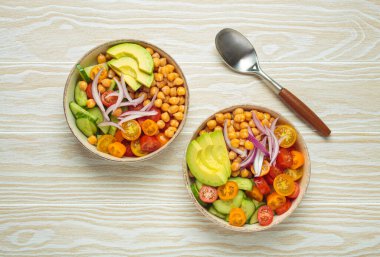 İki kase sağlıklı nohut salatası, olgun avokado, sulu vişneli domates, salatalık ve kırmızı soğan dilimleri. Besleyici ve sağlıklı bir yemek için mükemmel.