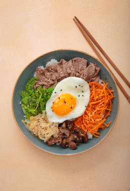 Bibimbap, haşlanmış pirinçli otantik Kore yemeği, kızarmış yumurta, sığır eti, renkli sebzeler, Kore 'nin geleneksel bej arka plan manzarası.