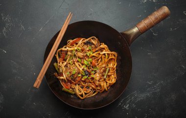 Tavada kızarmış tavuk ve sebzeli erişte, tepesinde tahta çubuklar, kırsal arka planda üst manzara.