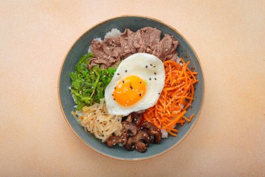 Bibimbap, haşlanmış pirinçli otantik Kore yemeği, kızarmış yumurta, sığır eti, renkli sebzeler, Kore 'nin geleneksel bej arka plan manzarası.