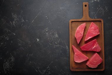 Taze kesilmiş ton balıklı biftekler yemek pişirmeye hazırlanıyor, tahta bir tahtadaki dilimler yazı için.
