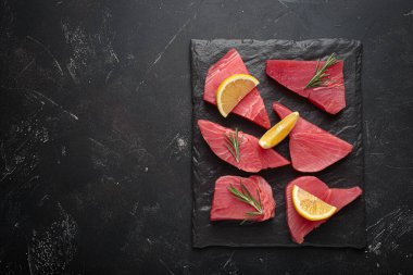 Taze kesilmiş ton balıklı biftekler pişmeye hazırlanıyor. Taze biberiye ve limon dilimleri ile tatlandırılmış.