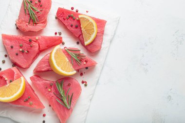 Beyaz arka planda taze çiğ ton balığı bifteği, limon dilimleri, biberiye filizi ve biber taneleri.
