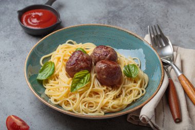 Üzerine köfte ve fesleğen yaprakları konmuş bir tabak spagetti, yanında domates sosu, çatal, kaşık, peçete ve domates dilimleri, sağlıklı ev yemekleri.