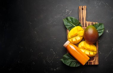 Mangolar, ahşap bir tahta üzerinde bir şişe ferahlatıcı meyve suyu ile, koyu arkaplan fotokopi alanı üzerine kuruludur.