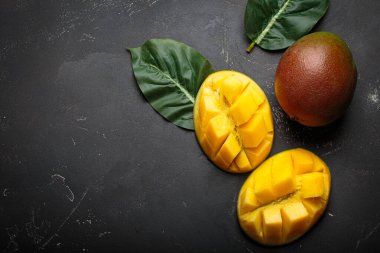 Siyah bir yüzeye yerleştirilmiş yeşil yapraklı tam ve dilimlenmiş taze mangolar sağlıklı bir yiyecek konsepti yaratıyor.
