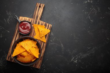 Koyu ahşap bir tahtaya daldırmak için kırmızı salsa soslu mısır tortilla cipsi. Yukarda düz bir meze sahnesi alanı var.