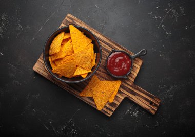 Koyu ahşap bir tahtaya daldırmak için kırmızı salsa soslu mısır tortilla cipsi.