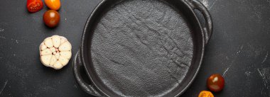 Taze sarımsak, domates, biberiye ve karışık biberiye ile çevrili koyu bir zemin üzerine demir tava dökmek