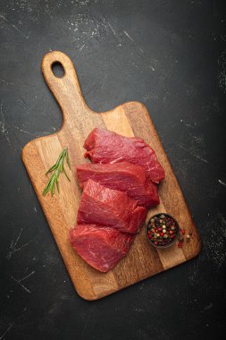 Tahta kesme tahtasında çiğ biftek, taze biberiye ve biberiye ile pişirilmeye hazır.