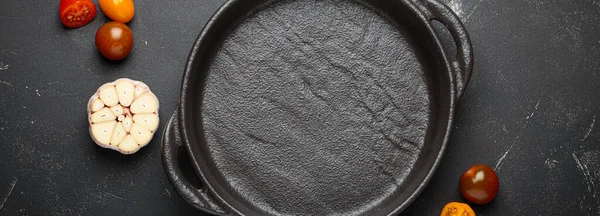 Taze sarımsak, domates, biberiye ve karışık biberiye ile çevrili koyu bir zemin üzerine demir tava dökmek