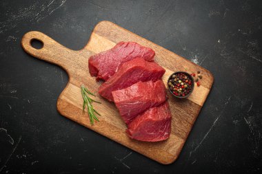 Tahta kesme tahtasında çiğ biftek, taze biberiye ve biberiye ile pişirilmeye hazır.