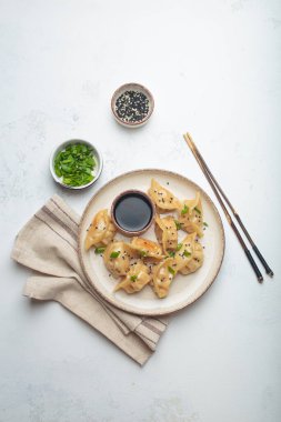 Soya sosu, doğranmış taze soğan, susam tohumu ve çubukla servis edilen pişirilmiş gyoza köftesi.