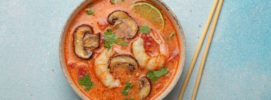 Karides, mantar, limon ve kişniş karışımlı lezzetli Tom çorbası mavi arka planda yemek çubuklarıyla servis edilen Tayland aromalı geleneksel bir yemektir.