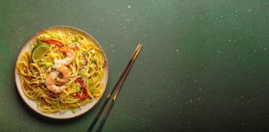 Karides, yer fıstığı, limon, kırmızı dolma biber ve yeşil soğanlı nefis Tayland eriştesi. Dokulu yeşil arkaplan, yemek çubukları üst görünümü, kopyalama alanı.