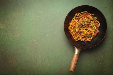 Tavada kızarmış tavuk ve sebzeli erişte, üstünde tahta çubuklar, yeşil arka planda üst manzara, kopyalama alanı