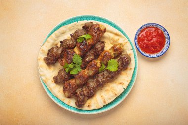 Izgara kofta kebabı domates soslu pide servis edilir ve renkli bir tabakta taze kişniş, canlı ve lezzetli bir orta doğu ya da Arap yemeği ile süslenir.