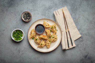 Soya sosu, doğranmış taze soğan, susam tohumu ve çubukla servis edilen pişirilmiş gyoza köftesi.