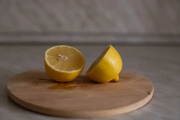 A yellow lemon is cut in half on a wooden cutting board. The cut lemon lies on the board.