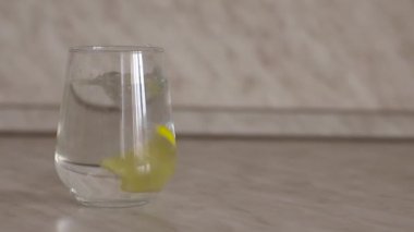 Bir dilim limon yavaş çekimde bir bardak suya düşer. Bir dilim limon yavaşça bir bardak içme suyuna atılır. Bir dilim limon yavaşça bir bardak suya düşer. Metin için yer.