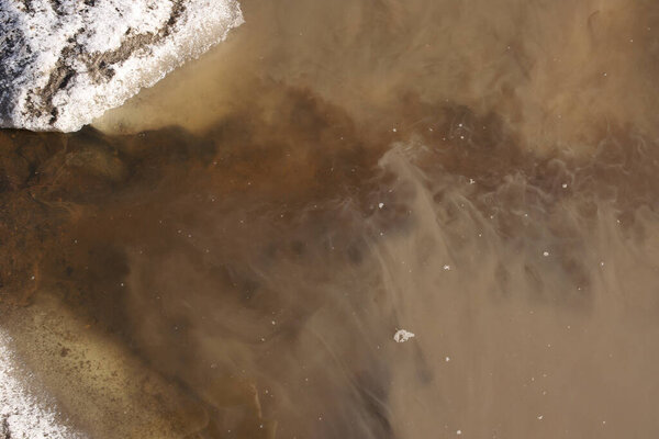 The stream of melt water flows into a muddy puddle in early spring. Pure water from the stream is mixed with a muddy puddle. Top view mixing different waters in spring.