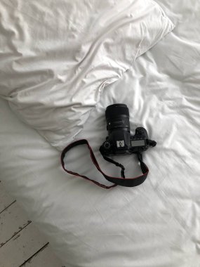 Siyah bir SLR kamera beyaz bir yatağın üzerinde duruyor. Kar beyazı bir yatakta, dikey bir fotoğraf makinesi var..