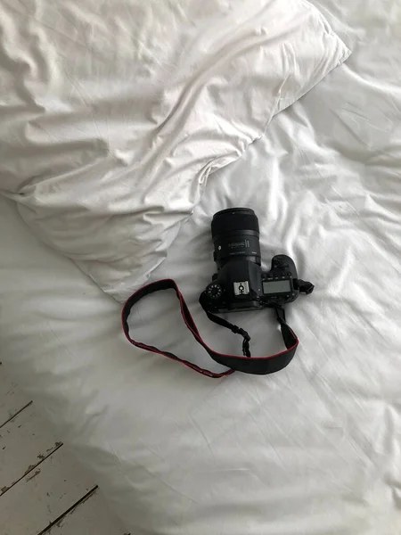 一架黑色的Slr相机矗立在一张白色的床上 俯瞰着全景 雪白的床上有一个摄像头 一张垂直的照片 图库图片