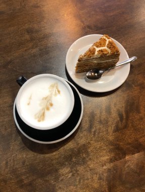 Ahşap bir masada köpüklü bir fincan kahve ve bir parça kahverengi kek var. Tatlı ve kahve koyu ahşap bir masada..