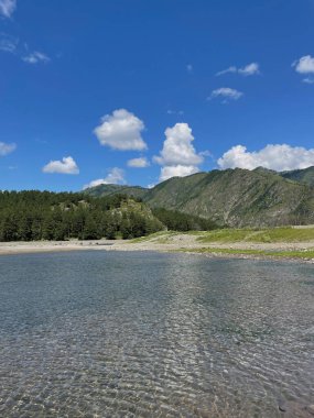 Dağların, mavi gökyüzünün ve kozalaklı ormanın arka planında temiz bir dağ gölünün pürüzsüz yüzeyi. Dikey fotoğraf, Altai Dağı, Altai Cumhuriyeti.