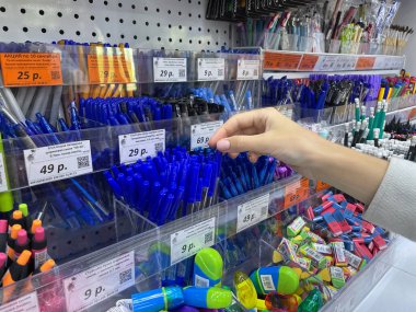 Kızın eli raftan yazmak için bir kalem alıyor. Ebeveynler okul çocukları için kırtasiye malzemesi alırlar. Kız bir kalem alır. Rusya, Altai Bölgesi, Barnaul, 08.16.2021