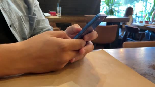 クローズアップ スマートフォンでページをめくるヨーロッパの男の手 電話のテープから喫茶店の若い男が出てくる — ストック動画