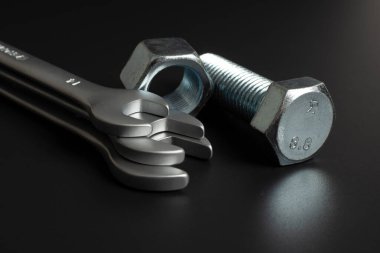 Birkaç büyük metal cıvata ve siyah arka planda anahtarlı fındık.