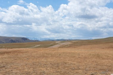 Bulutlu gökyüzünün arka planında küçük tepeler ve bozkırlar