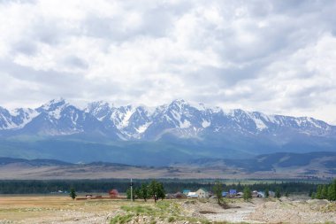 Dağların karlı zirveleri ve bulutlu gökyüzünün arka planında bozkır.
