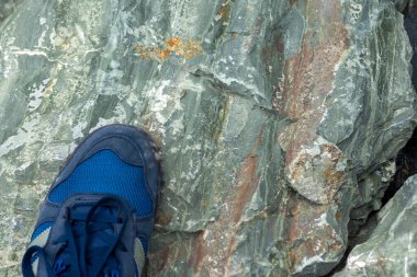 Büyük bir taşın üzerinde mavi ayakkabılı turist ayağı