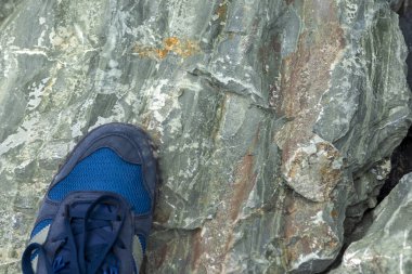 Büyük bir taşın üzerinde mavi ayakkabılı turist ayağı