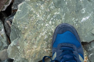 Büyük bir taşın üzerinde mavi ayakkabılı turist ayağı