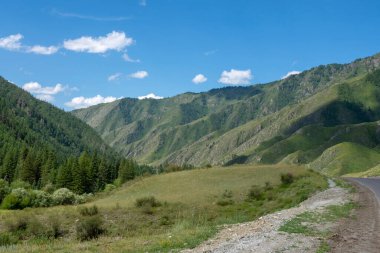 Bulutları ve otoyolu olan mavi gökyüzünün arka planındaki dağ zirveleri