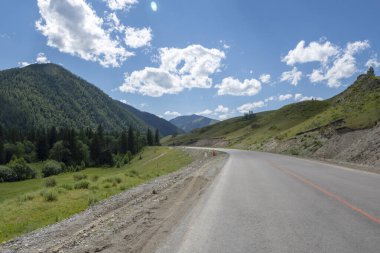 Bulutları ve otoyolu olan mavi gökyüzünün arka planındaki dağ zirveleri